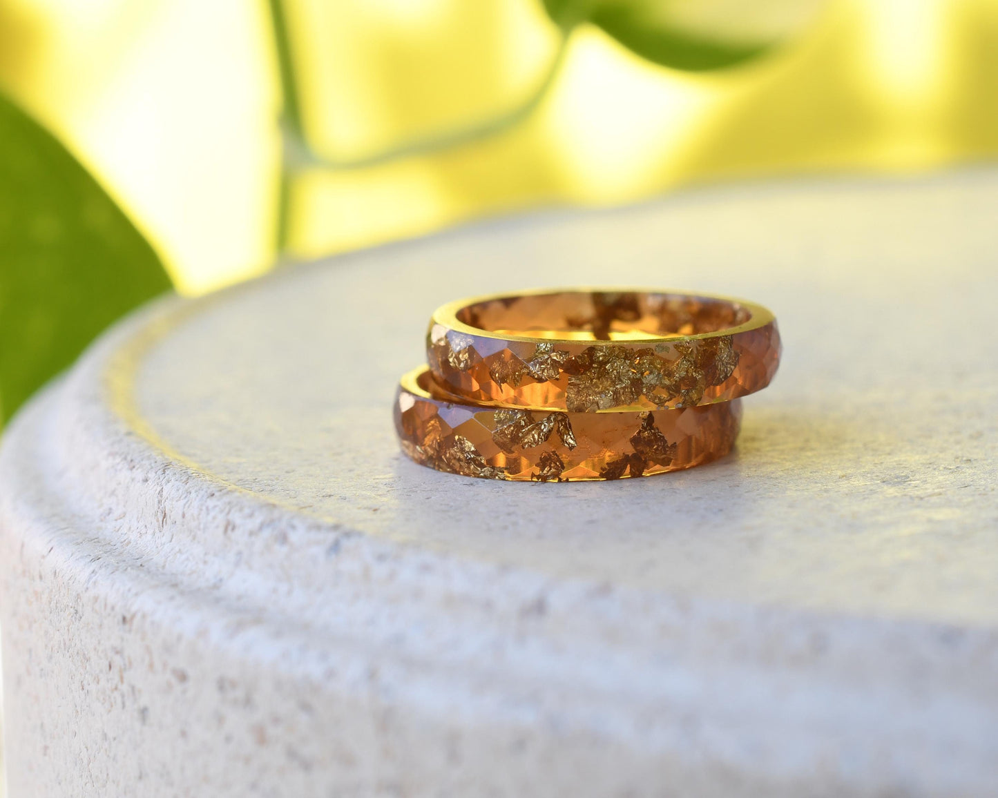 Two amber resin with gold rings on a white stone surface with a blurred green and yellow background
