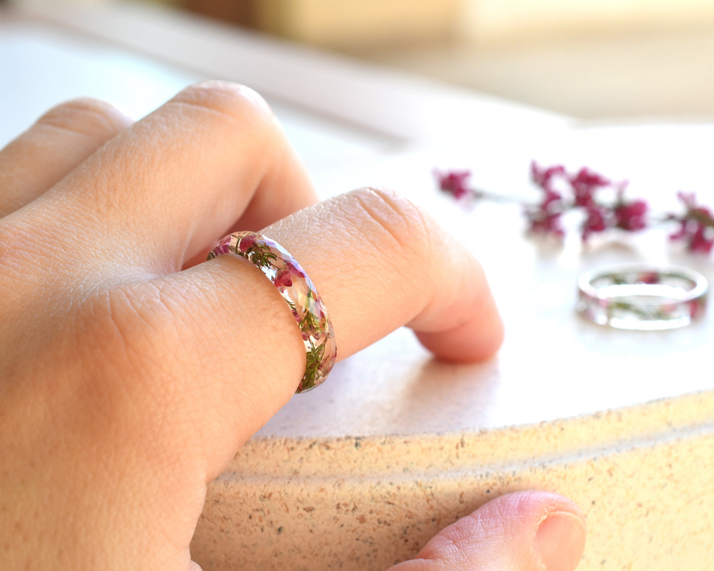 Faceted pink heather resin ring worn on hand