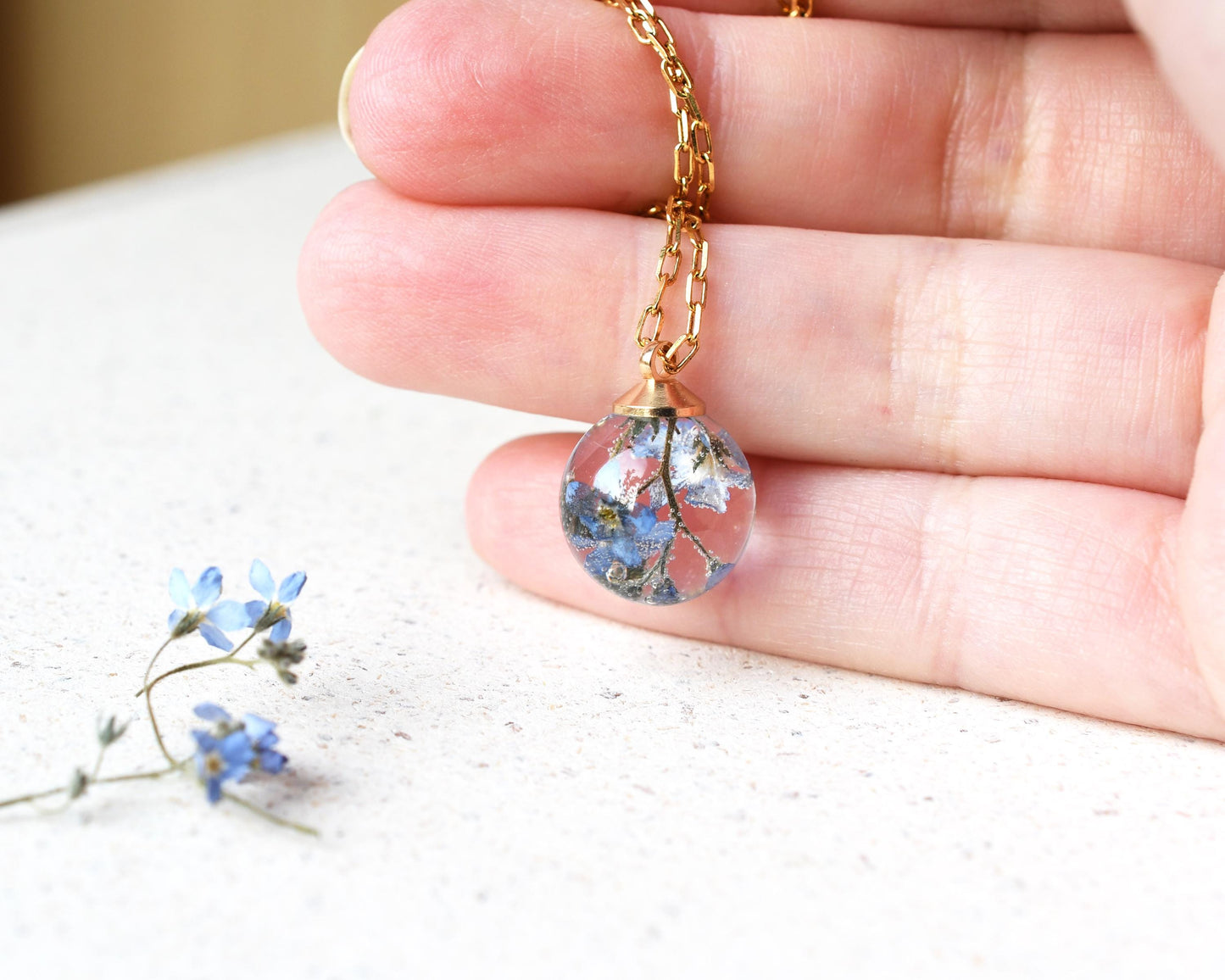 Necklace with a clear pendant containing dried flowers held by a hand on a light background