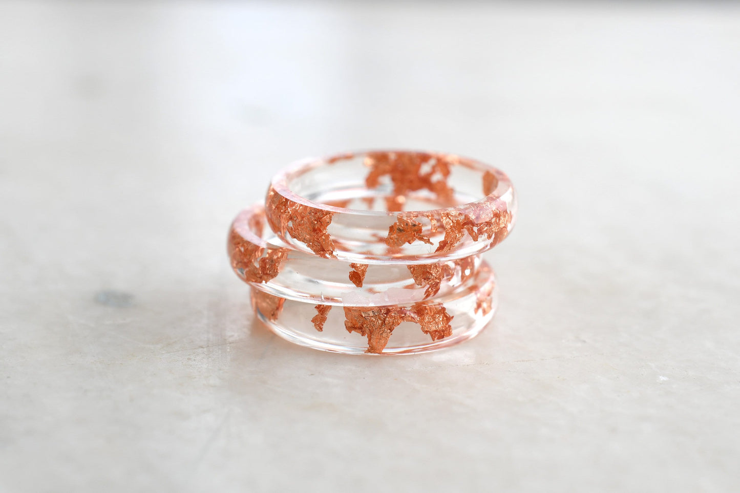 Stack of clear resin bracelets with red speckles on a light marble surface