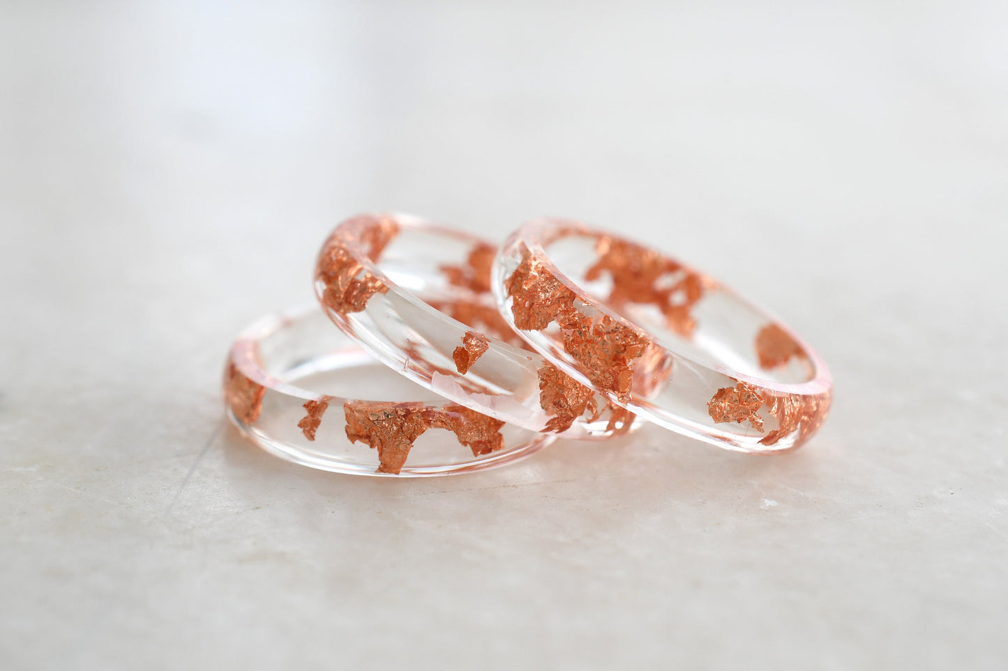 Two rose gold and clear resin rings on a light gray background