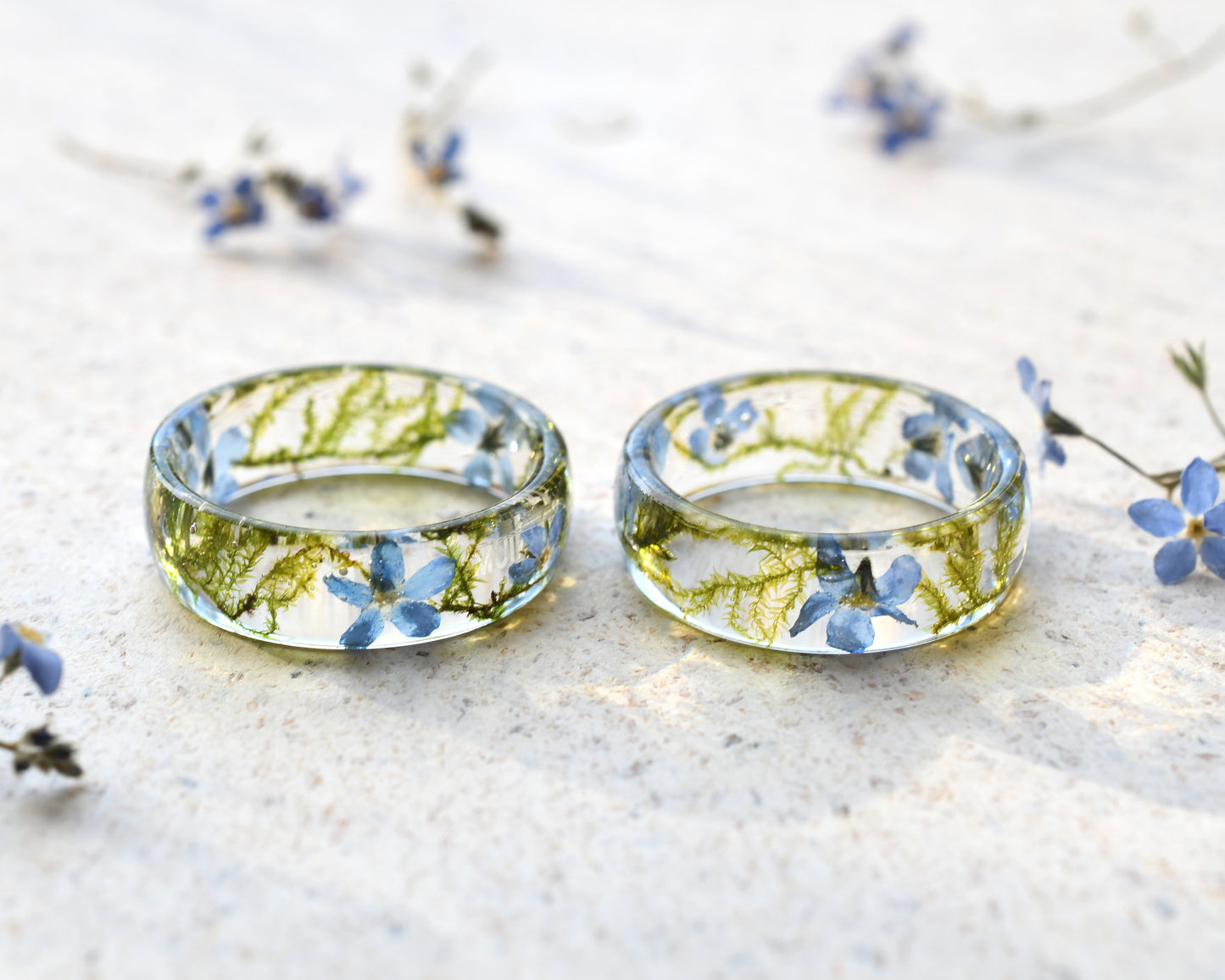 Two transparent rings with embedded flowers on a light surface.