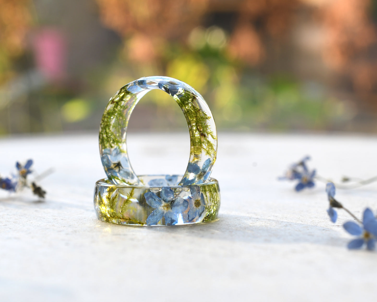 Two clear resin rings with embedded flowers on a light surface with blurred natural background