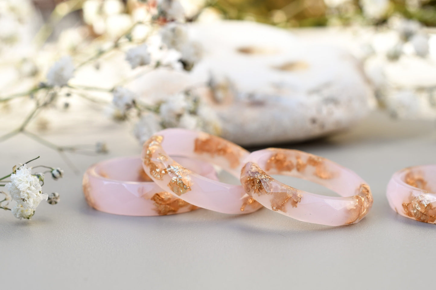 Three pink and gold rings on a light surface with blurred natural background