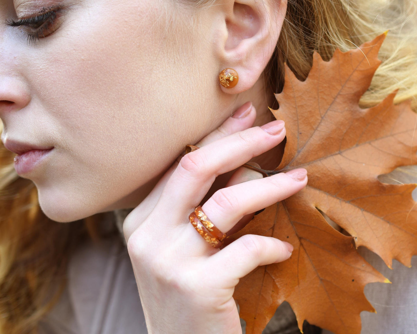 Woman wearing amber earrings with a close-up of her face and hand holding an autumn leaf.