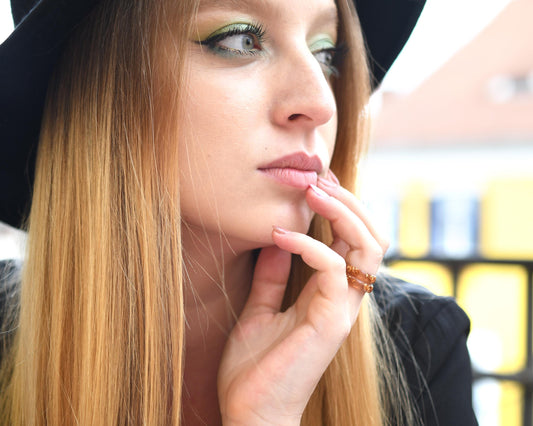Woman with long blonde hair and a black hat, wearing a black jacket, with a blurred background.