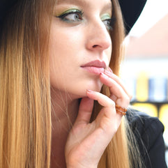 Woman with long blonde hair and a black hat, wearing a black jacket, with a blurred background.