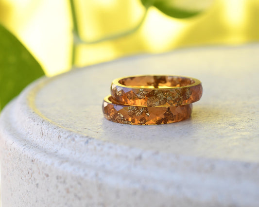 Two amber resin with gold rings on a white stone surface with a blurred green and yellow background