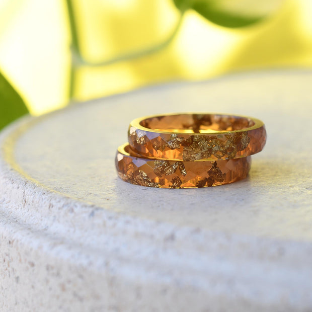 Two amber resin with gold rings on a white stone surface with a blurred green and yellow background