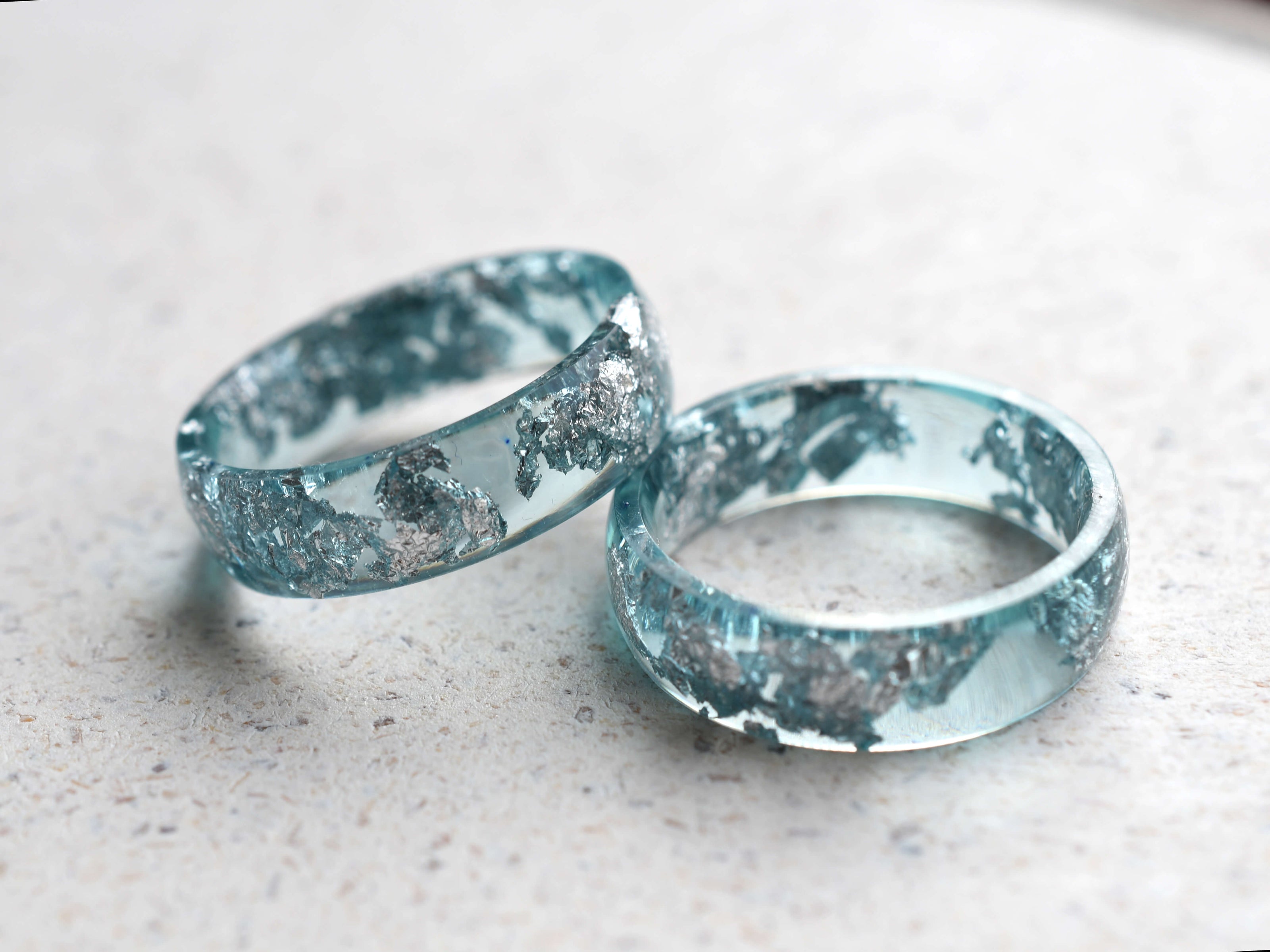 Two aquamarine resin rings with silver leaf accents on a light surface.