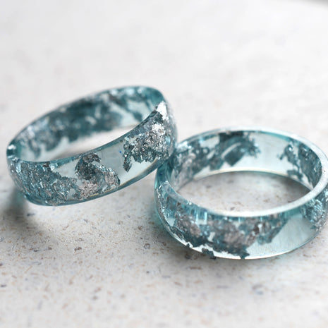 Two aquamarine resin rings with silver leaf accents on a light surface.
