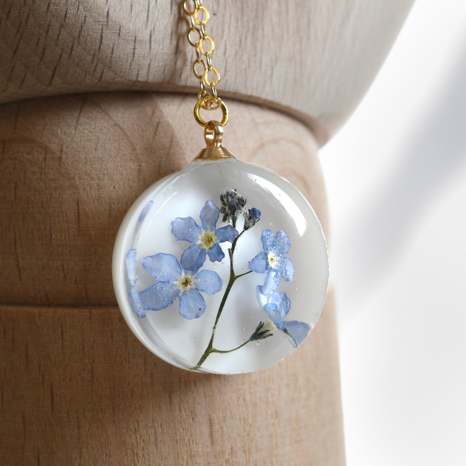 Real blue flower round resin necklace on white background — botanical jewelry