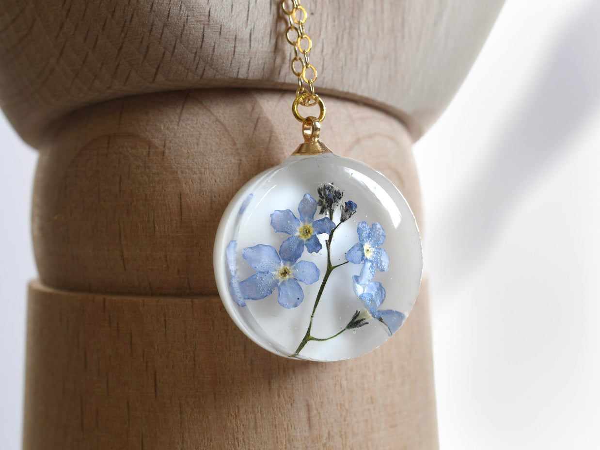 Real blue flower round resin necklace on white background — botanical jewelry