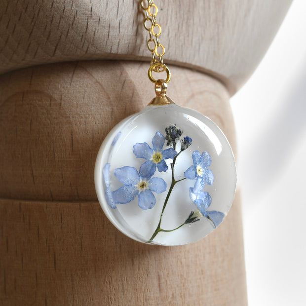 Real blue flower round resin necklace on white background — botanical jewelry