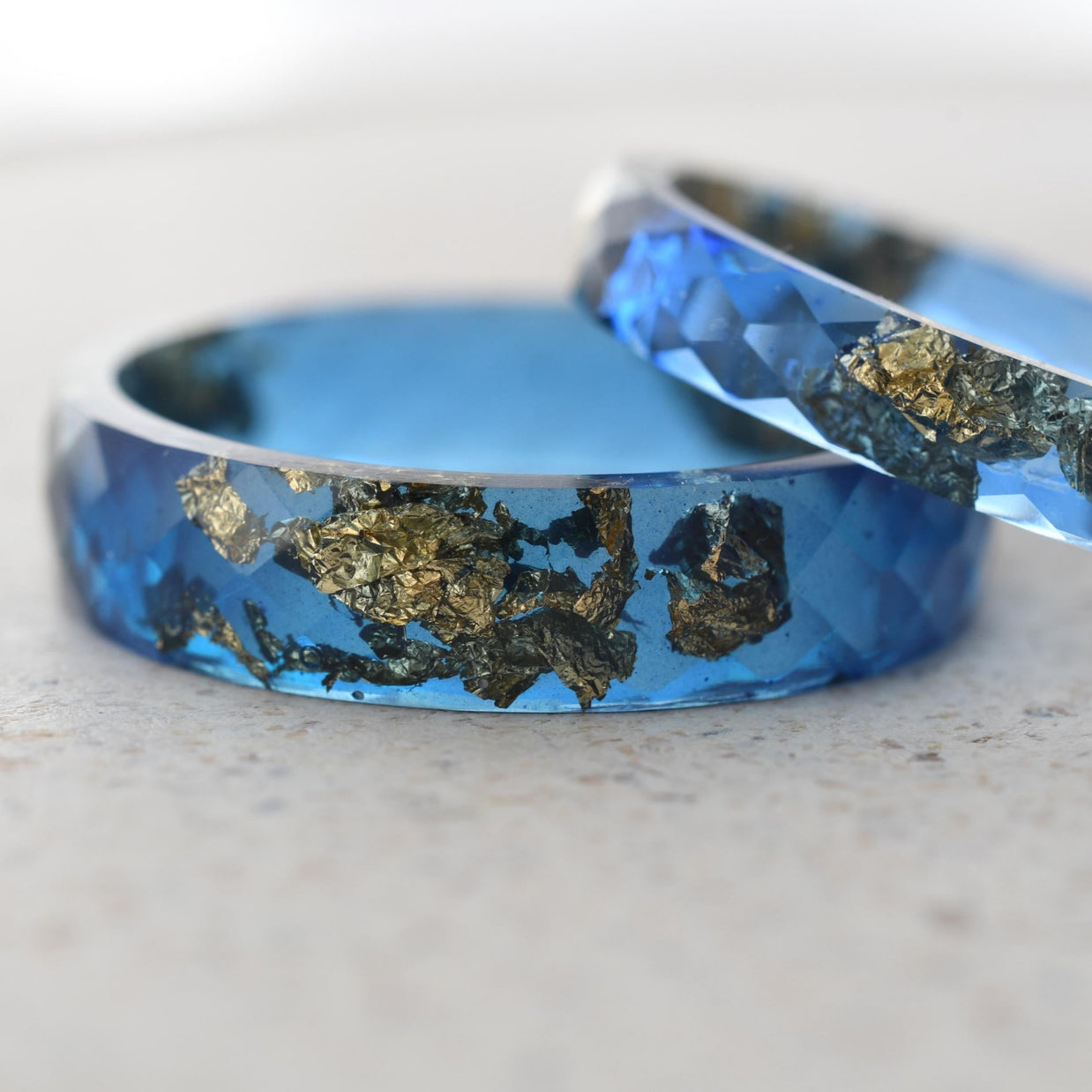 Close-up of sapphire blue resin with gold leaf flakes — faceted handmade rings
