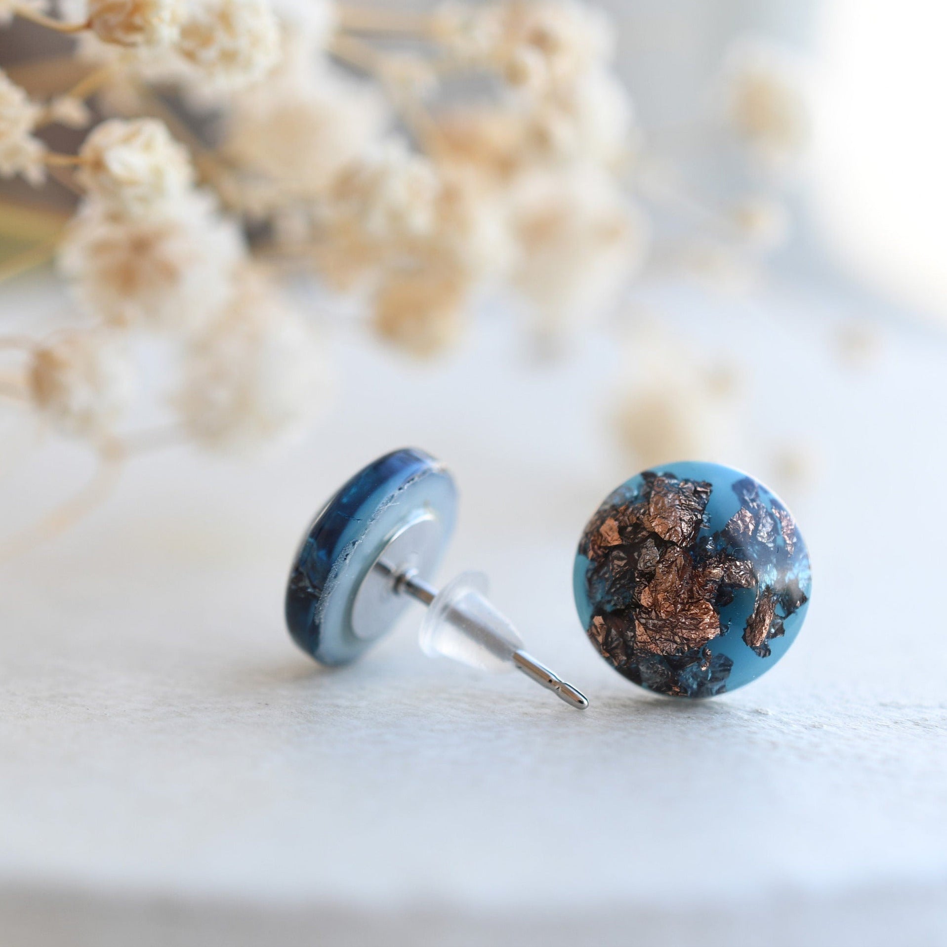 Close-up of blue pigmented resin earrings with shimmering rose gold flakes