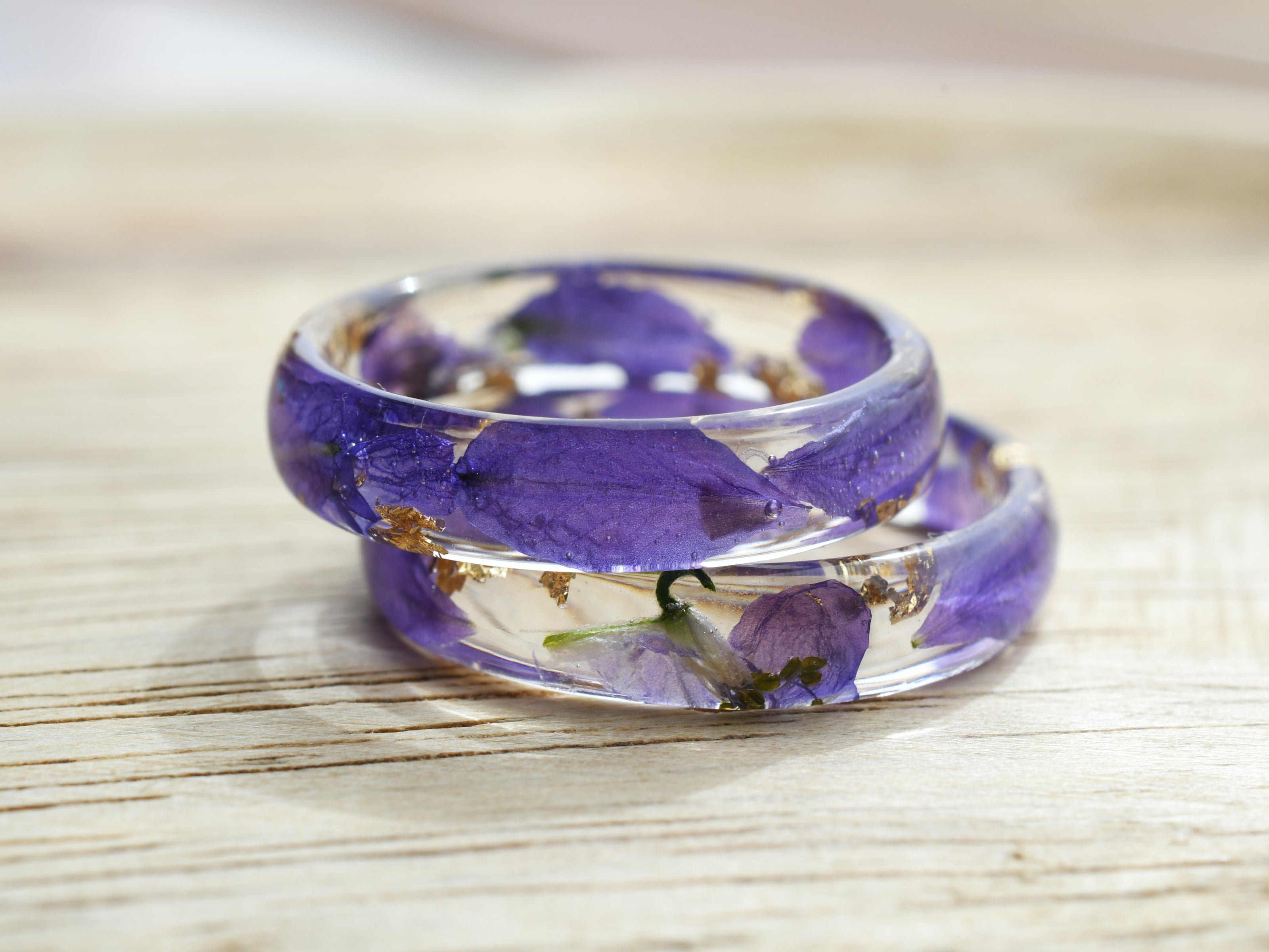 Resin ring with real violet larkspur petals, shown flat on natural wood background