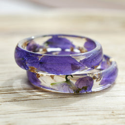 Resin ring with real violet larkspur petals, shown flat on natural wood background