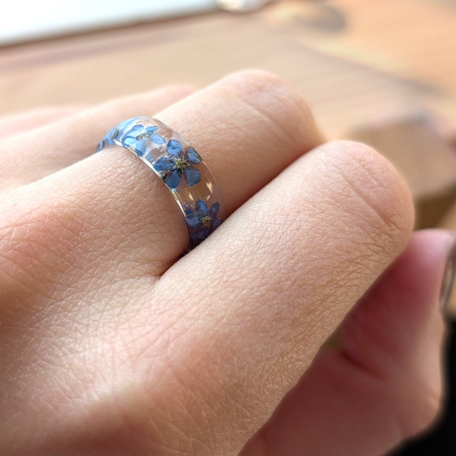 Close-up of a hand wearing a ring with blue floral design on a blurred background