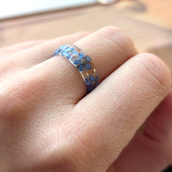 Close-up of a hand wearing a ring with blue floral design on a blurred background