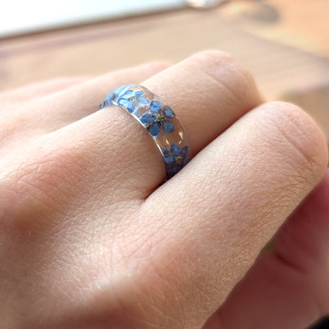 Close-up of a hand wearing a ring with blue floral design on a blurred background