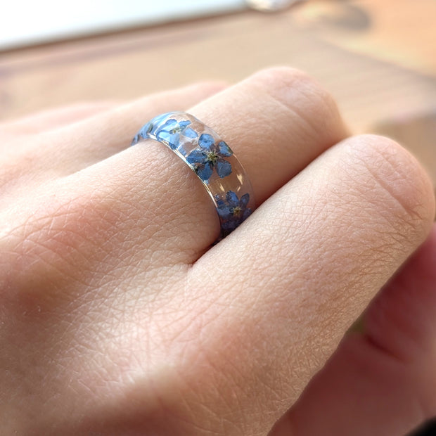 Close-up of a hand wearing a ring with blue floral design on a blurred background