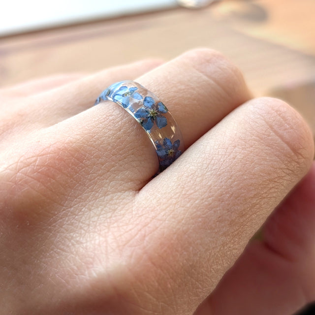 Close-up of a hand wearing a ring with blue floral design on a blurred background