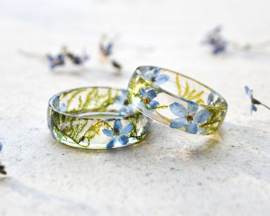 Two transparent resin rings with embedded blue flowers on a light background