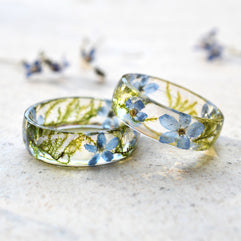 Two transparent resin rings with embedded blue flowers on a light background
