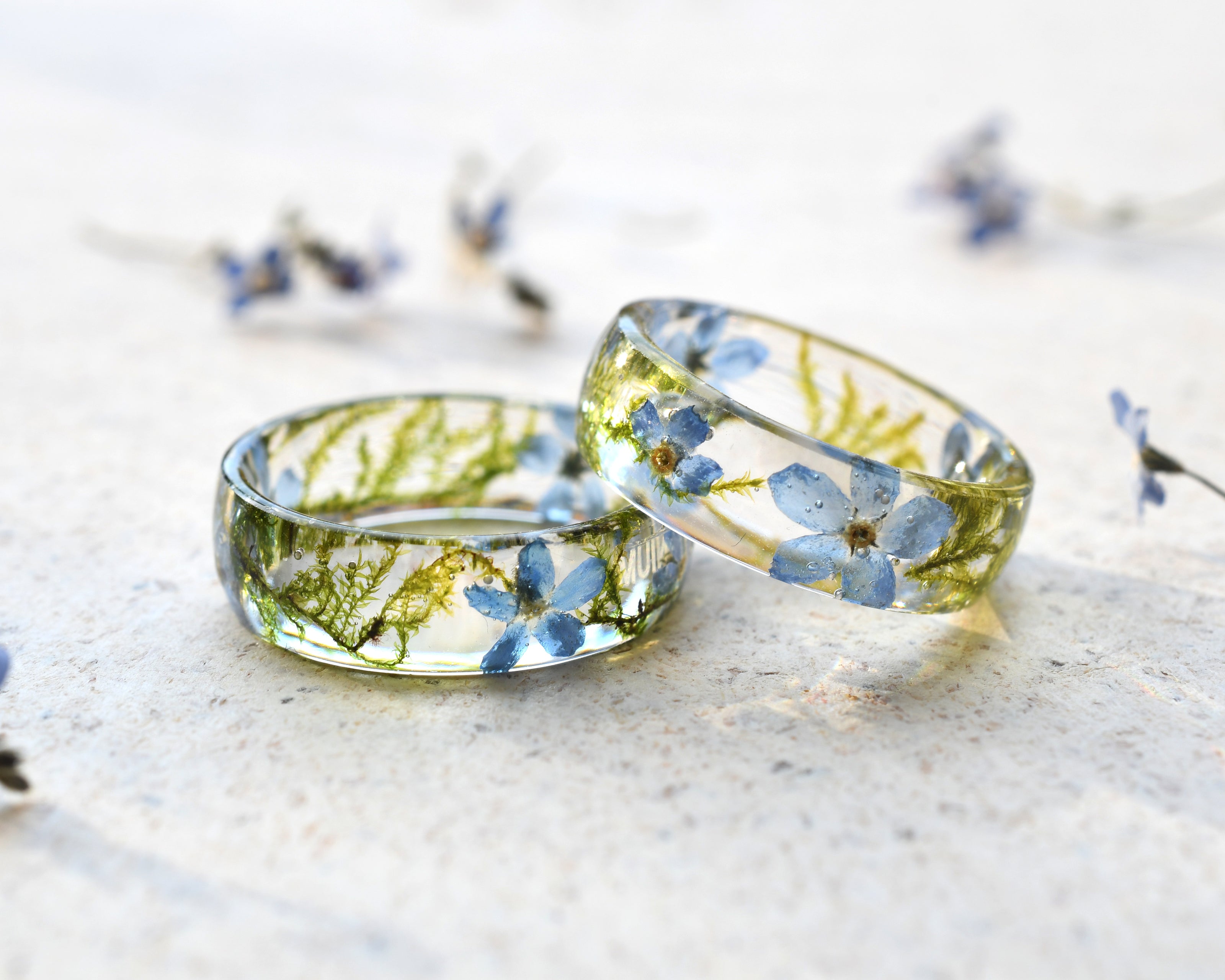 Two transparent resin rings with embedded blue flowers on a light background