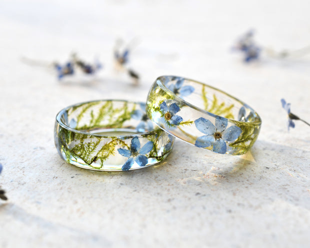 Two transparent resin rings with embedded blue flowers on a light background