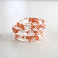 Stack of clear resin bracelets with red speckles on a light marble surface