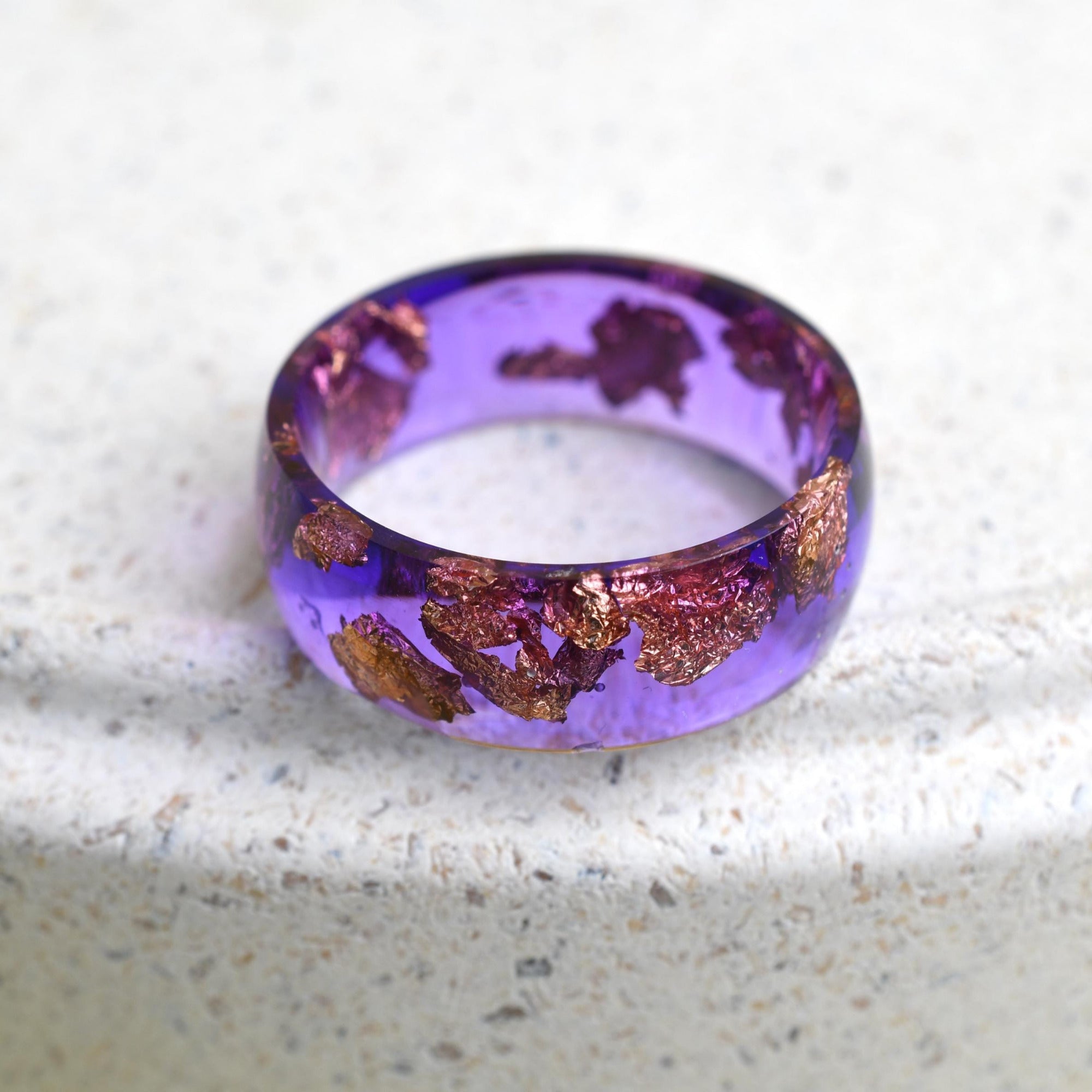 Close‑up of rose‑gold leaf being embedded in violet resin during hand‑crafting process.