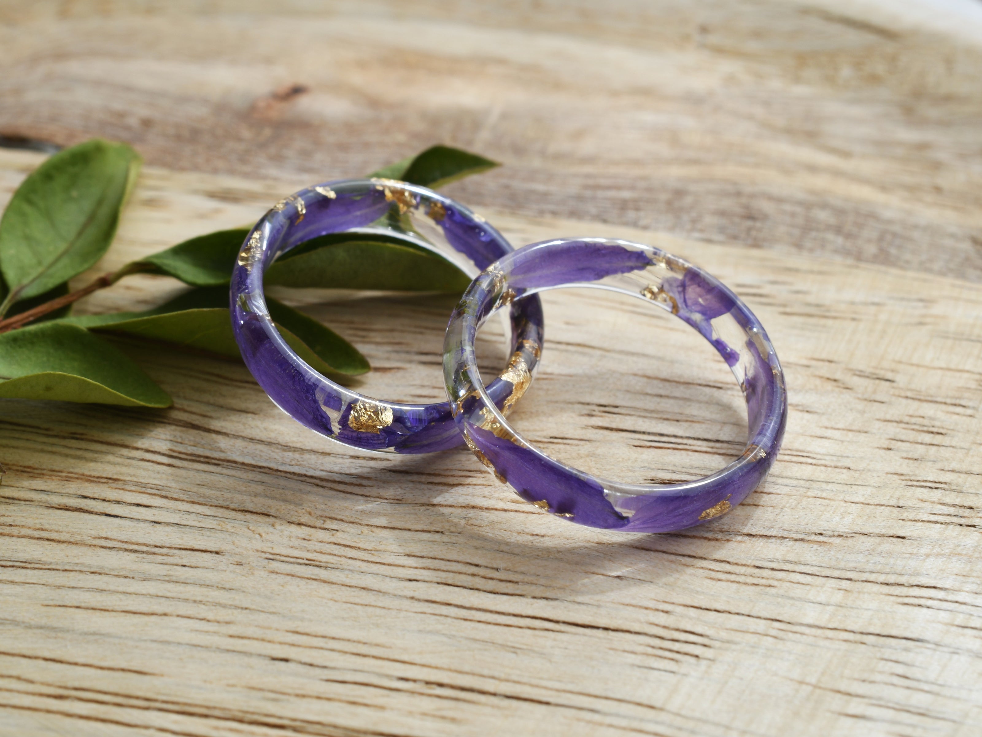Purple rings with gold accents on a wooden surface with green leaves.
