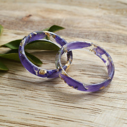 Purple rings with gold accents on a wooden surface with green leaves.