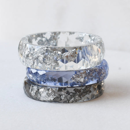 Two rings with textured silver bands and clear gemstones on a white background