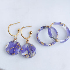 Pair of purple earrings with gold accents on a white surface