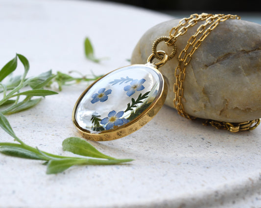 Handcrafted pendant featuring real dried forget-me-not flowers preserved in clear resin with a high-quality gold-plated finish.