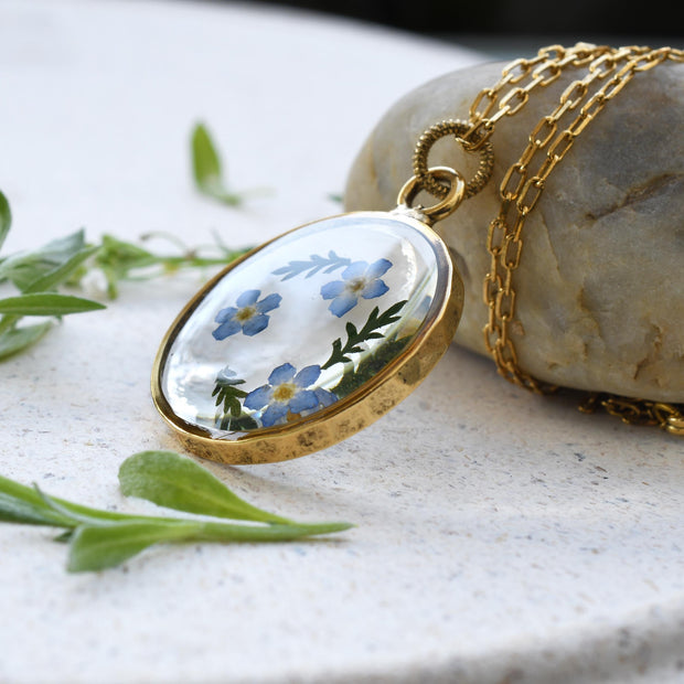 Handcrafted pendant featuring real dried forget-me-not flowers preserved in clear resin with a high-quality gold-plated finish.