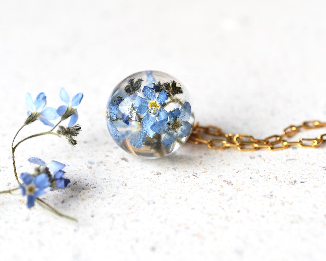 Necklace with a spherical pendant filled with blue flowers on a white background