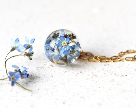Necklace with a spherical pendant filled with blue flowers on a white background