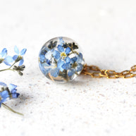 Necklace with a spherical pendant filled with blue flowers on a white background