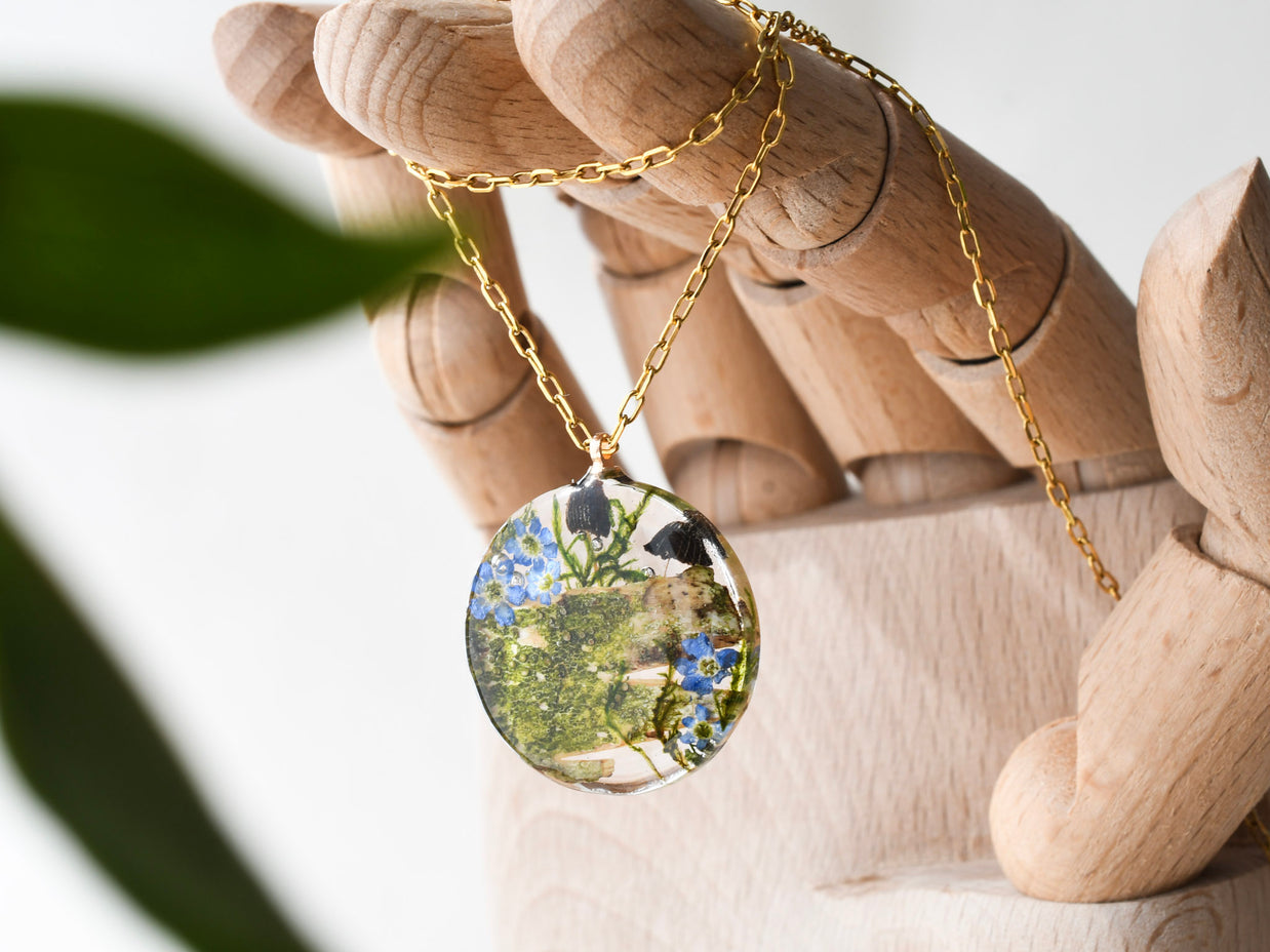 Close-up of forget-me-not flowers and mushrooms inside clear resin pendant