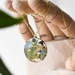 Close-up of forget-me-not flowers and mushrooms inside clear resin pendant