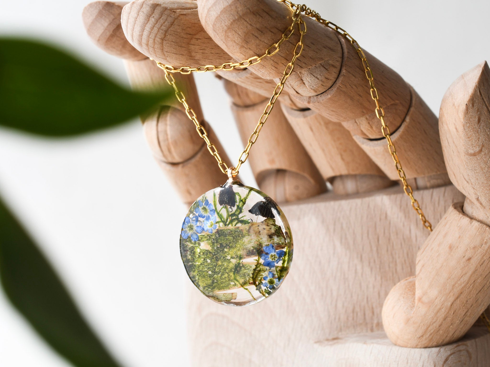 Close-up of forget-me-not flowers and mushrooms inside clear resin pendant