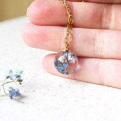 Necklace with a clear pendant containing dried flowers held by a hand on a light background