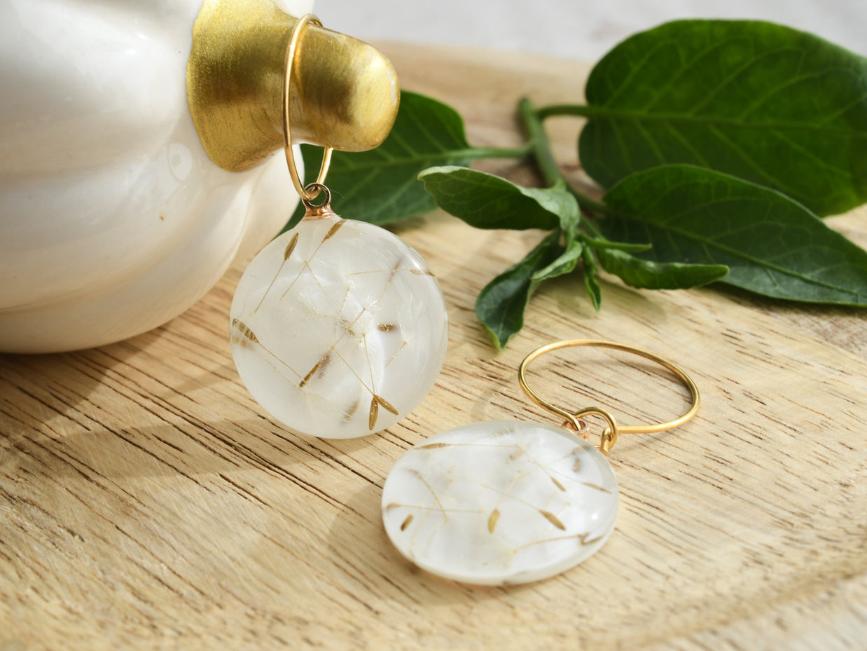 Close-up of handcrafted resin earrings with dried dandelion seeds on golden hoops, symbolic jewelry of wishes