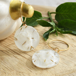 Close-up of handcrafted resin earrings with dried dandelion seeds on golden hoops, symbolic jewelry of wishes