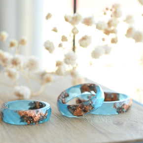 Three turquoise rings with copper inclusions on a wooden surface with decorative elements in the background.