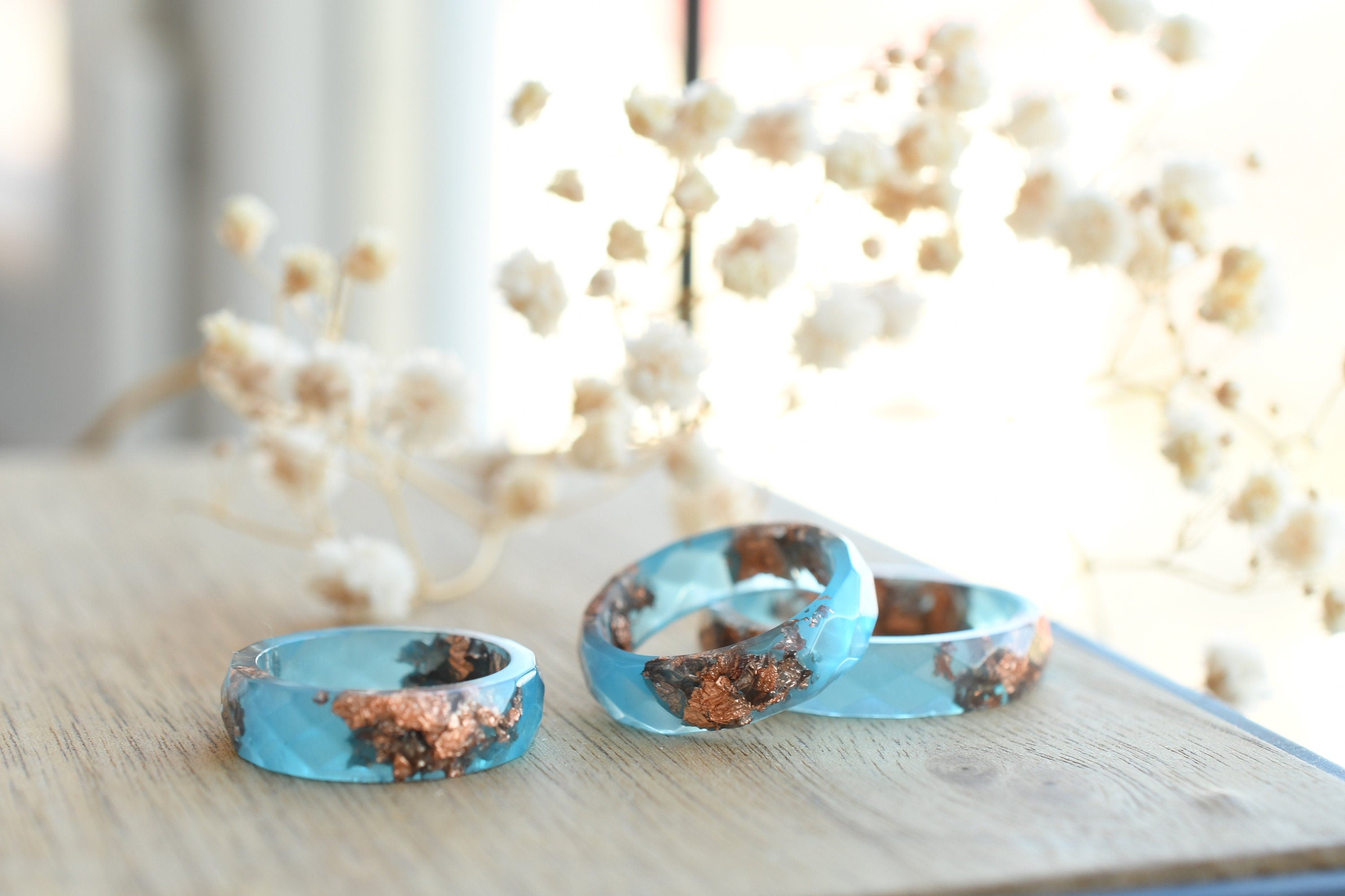Three turquoise rings with copper inclusions on a wooden surface with decorative elements in the background.